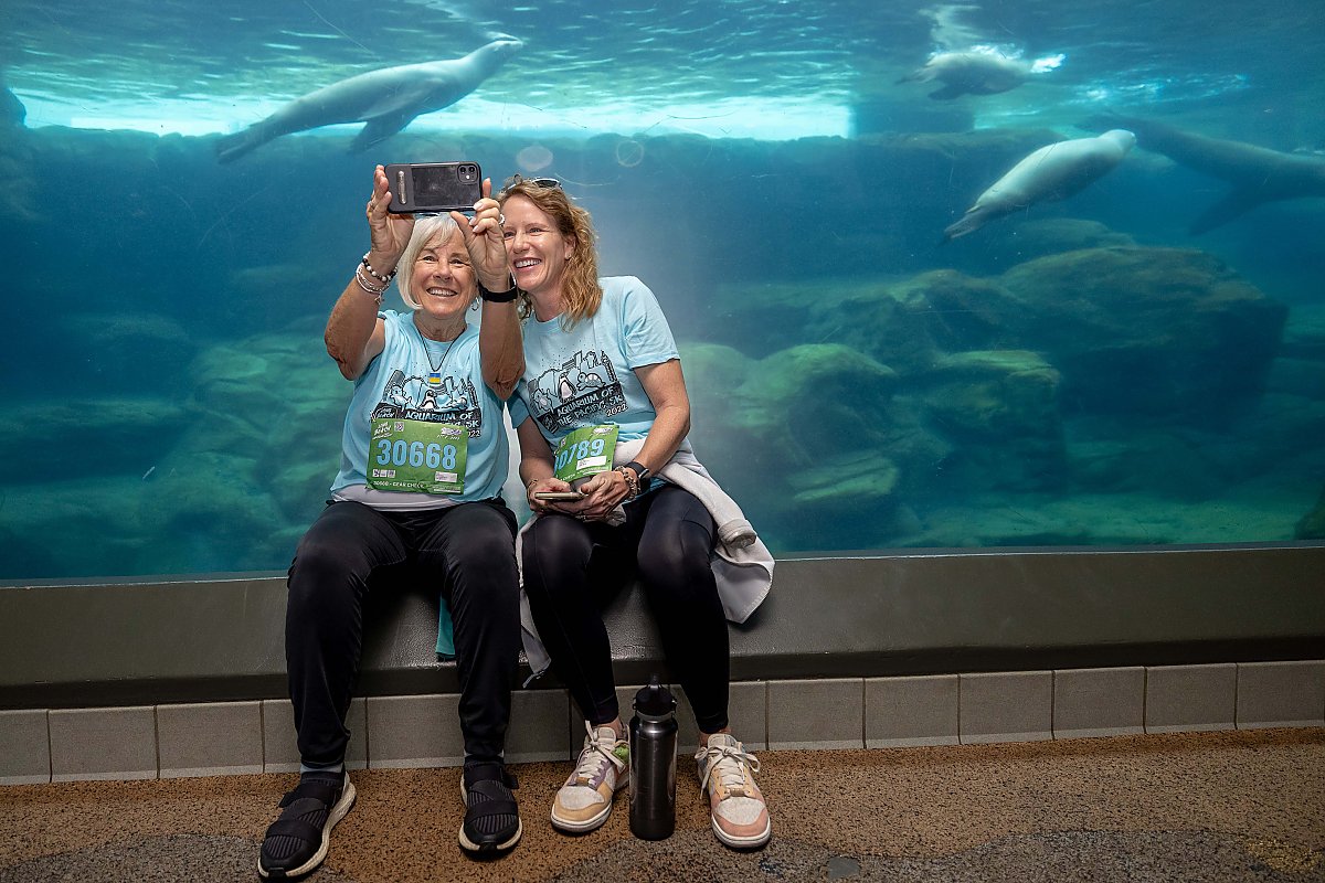 two women wearing race bibs sit to take a selfie in sea lion tunnel