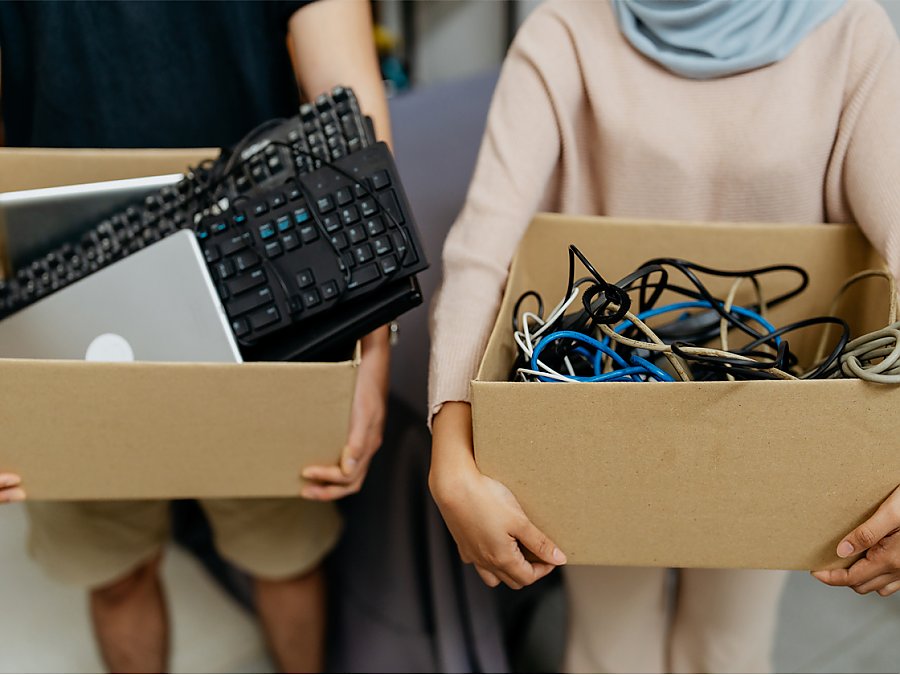 two people with cardboard boxes full of e-waste like cables and keyboards